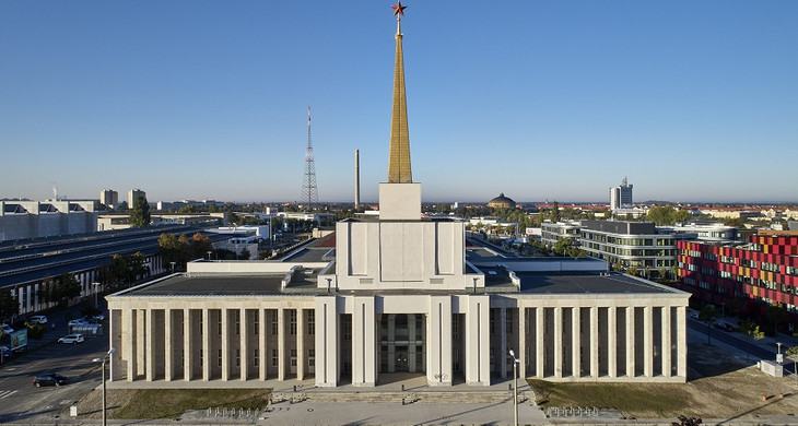 Gebäude des Stadtarchivs auf der Alten Messe, mit Säulengang und einer darauf thronenden goldenen, pyramidalen Spitze mit rotem Stern bekrönt ist.