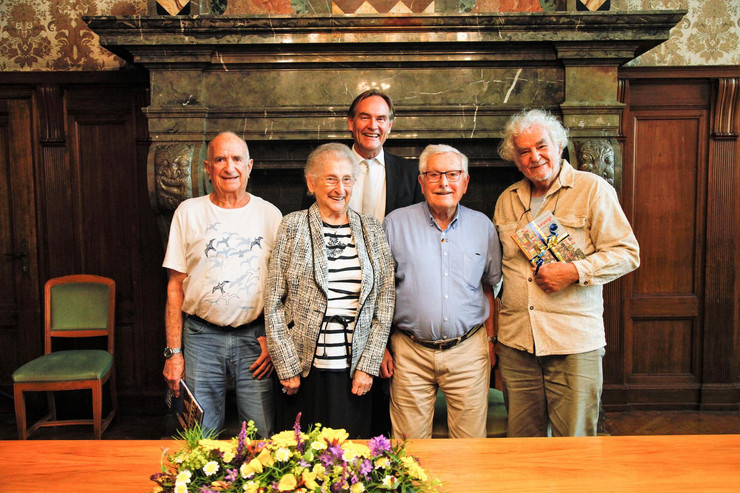 Drei ältere Herren und eine ältere Dame posieren mit Oberbürgermeister Jung für ein Foto, hinter ihnen der dunkelmarmorierte Kamin des Ratsplenarsaals, vor ihnen ein Tisch mit Blumengesteck.