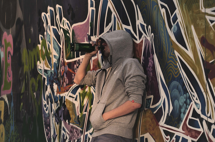 Ein junger Mann im Hoodie mit Schnapsflasche vor einer Graffiti-Wand