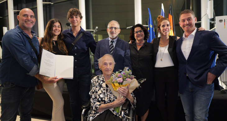 In der Mitte sitzt eine ältere Dame, die Ehrenbürgerin Channa Gildoni mit einem Blumenstrauß in der Hand. Um sie herum stehen sieben ihrer Familienmitglieder.