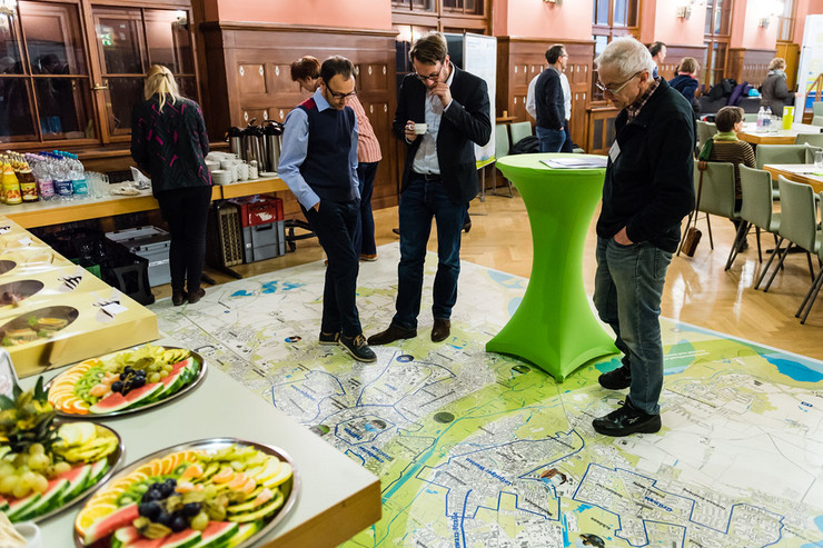 Blick auf das Catering, davor stehen Menschen auf einem Teppich. Auf dem Teppich ist ein Stadtplan von Leipzig eingezeichnet.