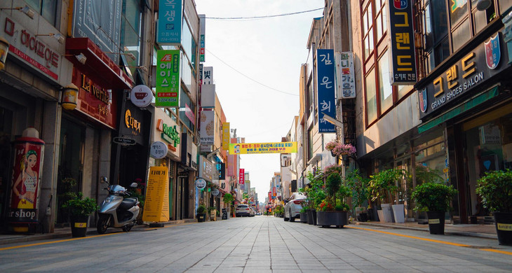Menschenleere Straße mit Shops an beiden Seiten, deren Werbetafeln in koreanischen Schriftzeichen gezeigt werden
