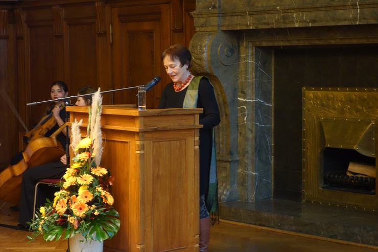 Professorin Dr. Godula Kosack steht hinter einem Stehpult und hält eine Rede. Vor dem Stehpult ist ein hoher Strauß Blumen.