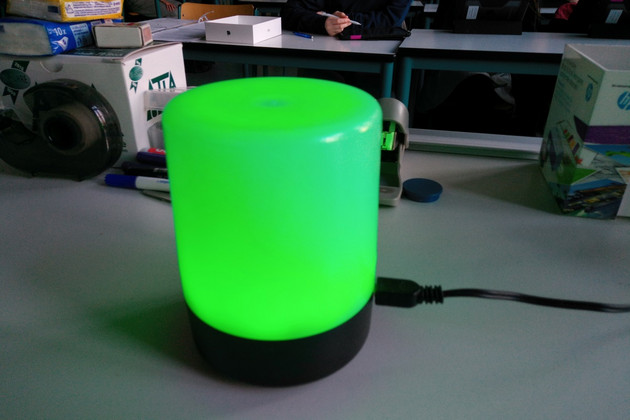 Eine CO2-Ampel, sieht aus wie eine zylinderförmige Lampe, steht auf einem Tisch und leuchtet grün.