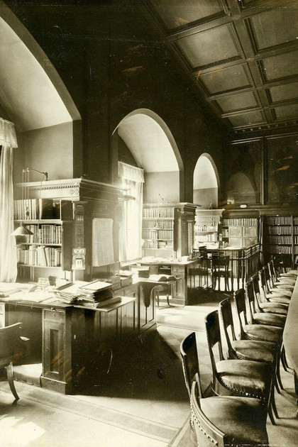 Zu sehen ist die Ratsstube im Alten Rathaus Leipzig mit den Arbeitsplätzen für Referendare und Assessoren, die sich auf der linken Bildseite befinden und jeweils im 90-Grad-Winkel zu den Fenstern stehen. Rechts im Bild befindet sich ein langer Tisch mit vielen Stühlen. Das Bild entstand um 1905.