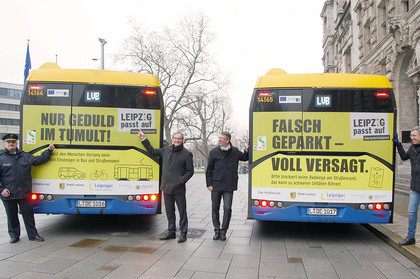 Vier Herren posieren an zwei Bussen der Leipziger Verkehrsbetriebe, die mit Motiven der Verkehrssicherheitskampagne beklebt sind
