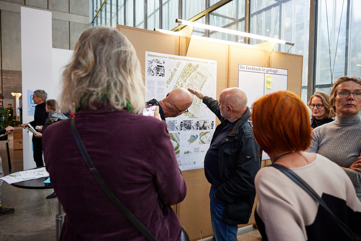 Menschen schauen auf ein Plakat eines städtebaulichen Entwurfs und diskutieren