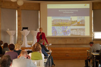 Eine Rednerin zeigt in einem Saal mit Publikum eine Präsentation zum Thema Monitoring im Stadtumbau