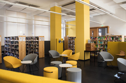 Gelbe und graue Stühle und Sitzhocker mit kleinen Tischen vor großen Bücherregalen