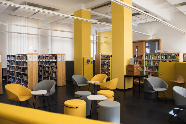 Gelbe und graue Stühle und Sitzhocker mit kleinen Tischen vor großen Bücherregalen