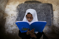 Afghanisches Mädchen mit weißem Kopftuch liest aus blauem Buch vor