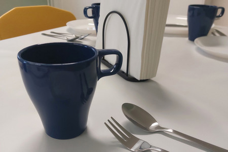 Auf dem Bild sind beispielhaft für eine Kaffeetafel ein Teller, Besteck, eine Tasse und Servietten auf einem Tisch zu sehen.