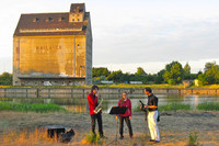 Drei Musiker am Lindenauer Hafen. In Hintergrund eines der großen Speichergebäude.