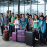 Gruppenfoto vorm gläsernen Eingang zum Flughafen mit Schülern und Koffern
