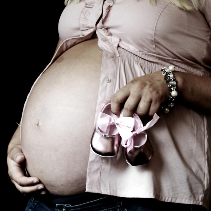 Schwangere mit dickem Bauch und Babyschuhchen in der Hand