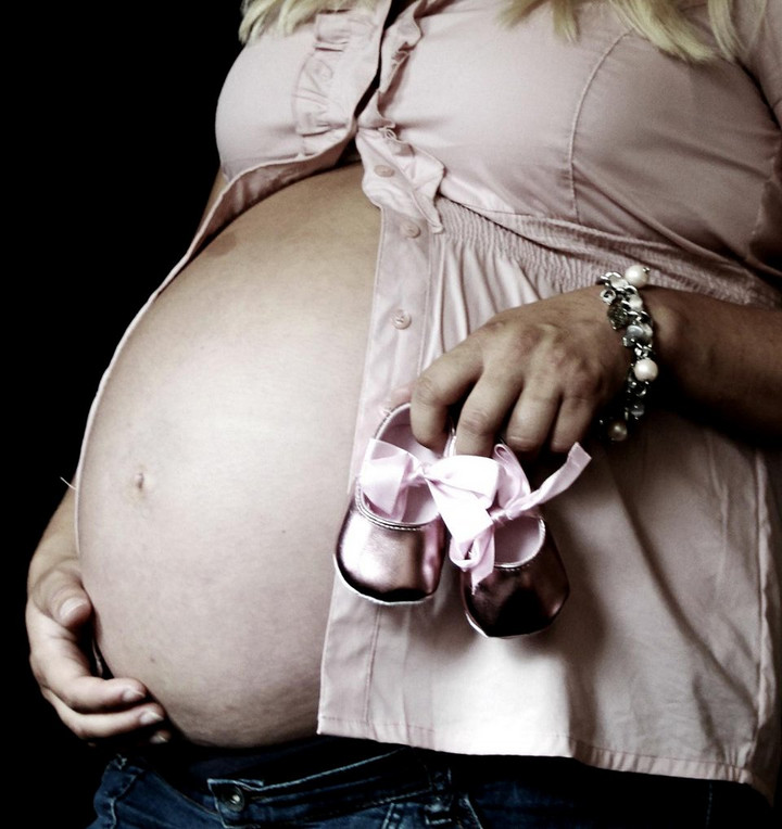 Schwangere mit dickem Bauch und Babyschuhchen in der Hand