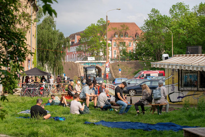 Menschen sitzen auf Bänken und Decken am Polygraphplatz, wo der Ostwache e. V. und Sphere Radio ein buntes Programm zum Tag der Städtebauförderung organisiert haben.