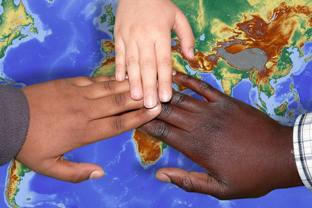 Weltkarte auf der sich drei Hände dreier Menschen mit verschiedenen Hautfarben berühren.