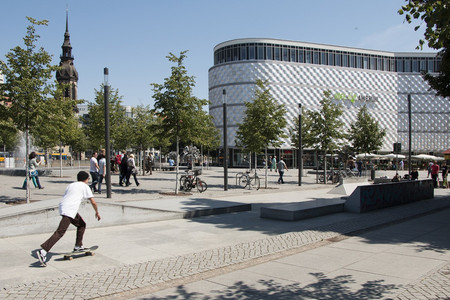 Richard-Wagner-Platz vor den Höfen am Brühl mit einem Skater, Passanten und vielen jungen Bäumen.