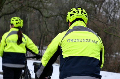 Eine Fahrradfahrerin und ein Fahrradfahrer von hinten mit gelben Westen und der Aufschrift "Ordnungsamt" 