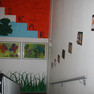 Der Treppenaufgang ist mit einem Frosch und dem Schriftzug OSKAR bemalt. Darunter hängen zwei von Kindern gestaltete Bilder. Über dem Treppengeländer sind Keramiken in Bildform aufgehängt.