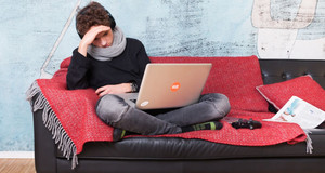 Ein Junge sitzt mit seinem Laptop auf einem roten Sofa