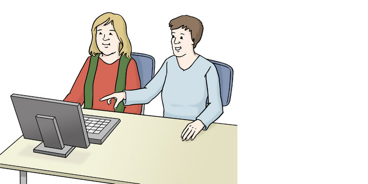 Zwei Personen sitzen an einem Schreibtisch vor einem Computerbildschirm. Eine Person zeigt auf den Bildschirm, die andere schaut zu.