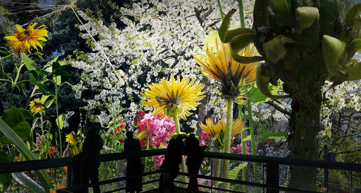 Besucher betrachten ein Gartenbild mit Blumen und einem blühenden Baum, das extrem vergrößert ist.
