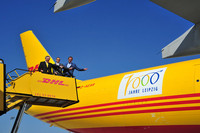 Oberbürgermeister Burkhard Jung und zwei DHL-Geschäftsführer stehen auf einer Rolltreppe am DHL-Frachtflieger und zeigen auf das große 1000-Jahre-Logo am gelben Rumpf des Flugzeuges.