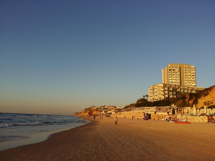 Blick auf den Strand und das Meer, blauer Himmel; Strand und Gebäude werden durch den Sonnenuntergang orange angestrahlt