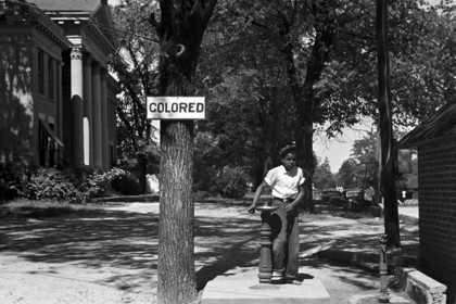 Ein Junge an einer Säule, daneben ein Zettel an einem Baum mit der Aufschrift "Colored"