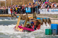 Ein Mann und eine Frau fahren in einem selbst gebauten Boot aus Pappe im Wildwasserkanal, im Hintergrund viele Zuschauer.