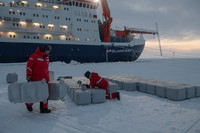 Rot gekleidete Menschen beim Aufbau der Stadt in der Arktis, im Hintergrund das Forschungsschiff Polarstern.