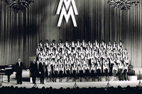 Schwarz Weiß Foto von 1977 mit einem Kinderchor auf einer großen Bühne. Über dem Chor hängt das Doppel-M als Zeichen der Leipziger Messe.