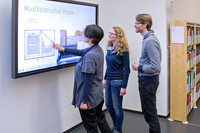 Drei personen stehen vor dem großen Touchscreen Monitor in der Stadtbibliothek und entdecken die multimediale Präsentation der Musikbibliothek Peters