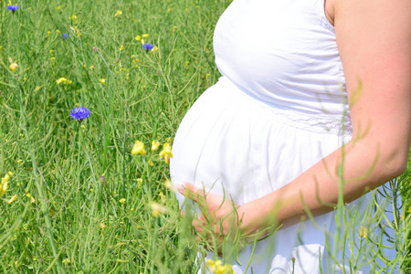 eine schwangere Frau mit weißem Kleid steht auf einer Sommerwiese