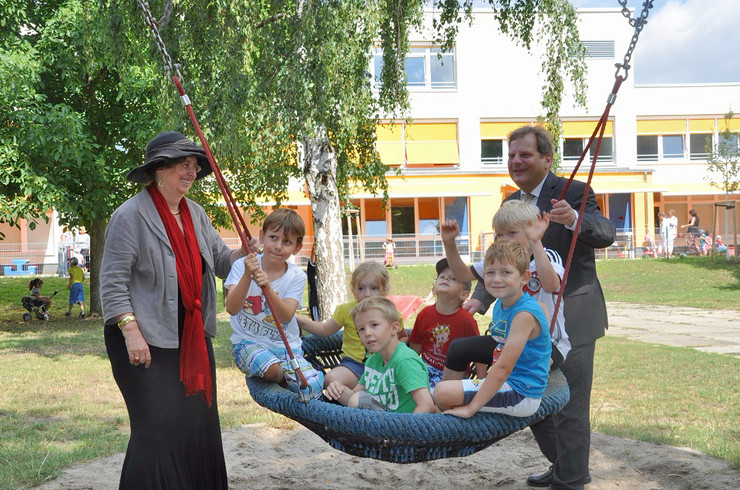 Baubürgermeisterin Dubrau und Sozialbürgermeister Fabian schaukeln eine Gruppe Kinder im Garten der Kita An der Lehde 12 - 14.