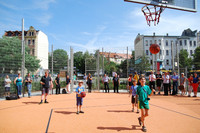 Kinder werfen Ball auf Basketballkorb, im Hintergrund stehen Menschen