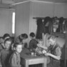Frauen und Kinder an einem Tisch im Innenraum der Baracke des Umsiedlungslagers mit Doppelstockbett im Hintergrund