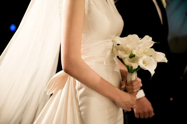 Braut mit Brautstrauß, im Hintergrund der Bräutigam