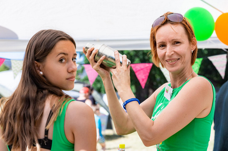 Eine Jugendliche und eine Frau, beide in grünen T-Shirts. Die Frau hält einen Shaker in den Händen.