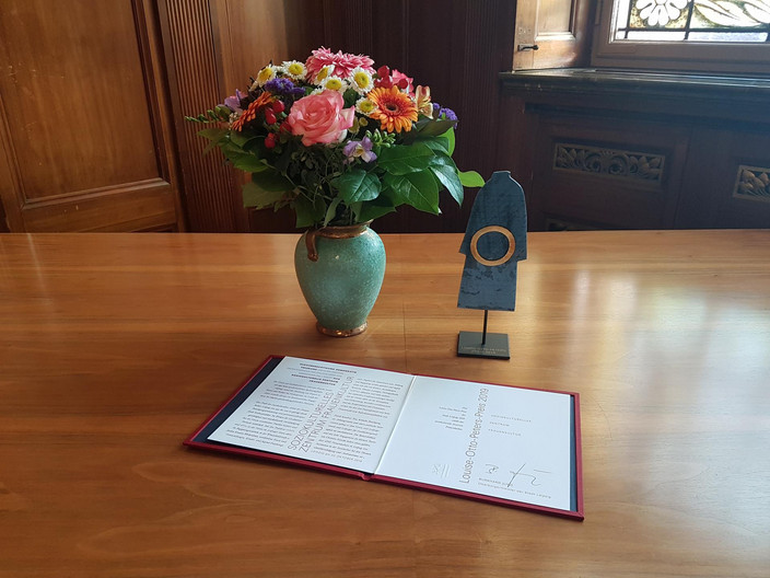 Urkunde, Blumenstrauß und Kunstgegenstand des Louise-Otto-Peters-Preises auf einem Holztisch