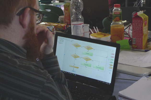 Blick über die Schulter eines Mannes auf einen Laptopbildschirm, auf dem ein Programmierplan zu sehen ist