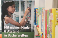 Plakat mit einem Mädchen welches ein Buch aus einem Bibliotheksregal nimmt