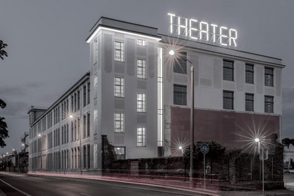 Blick auf das mehrstöckige, helle Gebäude in der Dämmerung mit beleuchtetem Schriftzug 'Theater'