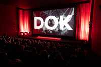 Blick in einen vollbesetzten Kinosaal, auf der Leinwand steht Dok in großen weißen Buchstaben