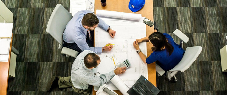 Eine Gruppe unterhält sich gemeinsam am Tisch und plant ein Bauvorhaben an einem Bauplan