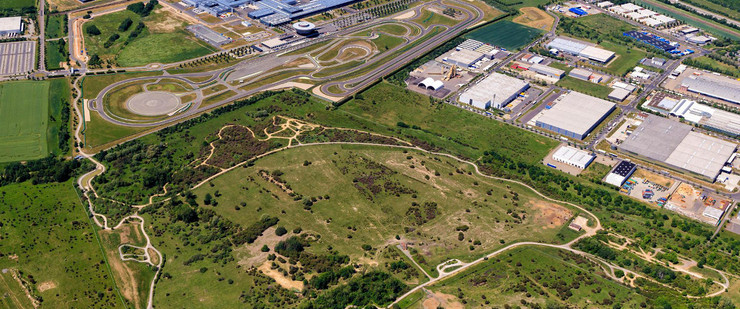 Luftbild des Werksgeländes von Porsche in Leipzig mit vielen Werkshallen, einer Testrennstrecke und Grünflächen.