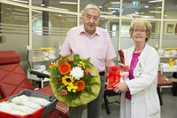 Ein alter Mann hält einen Blumenstrauß in der Hand. Neben ihm steht eine Ärztin im weißen Kittel und überreicht ihm ein Geschenk.