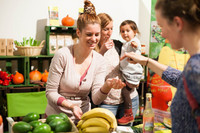 Eine Frau verkauft Obst. Im Hintergrund steht eine weitere Frau mit einem Kind auf dem Arm.